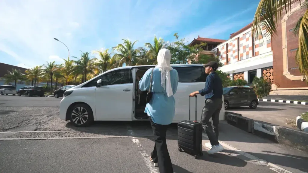 A guest with luggage and a driver walking to a white Alphard in Bali