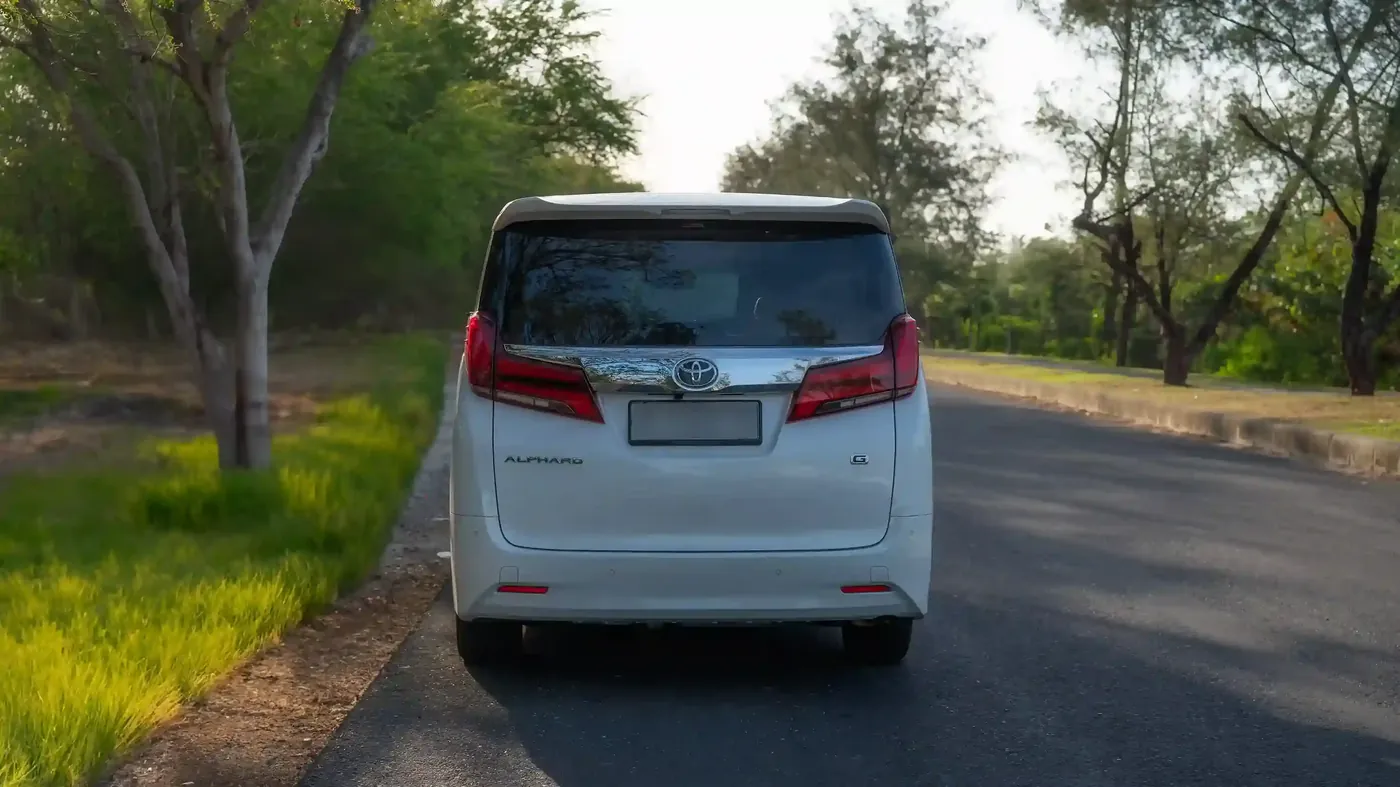 A white Alphard seen from behind on a tree-lined road
