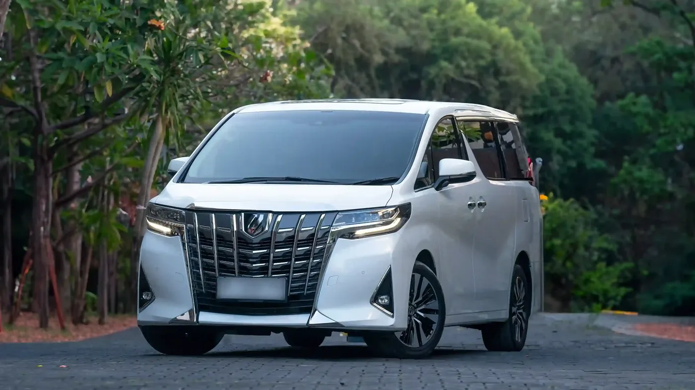 A white Toyota Alphard on a tree-lined road