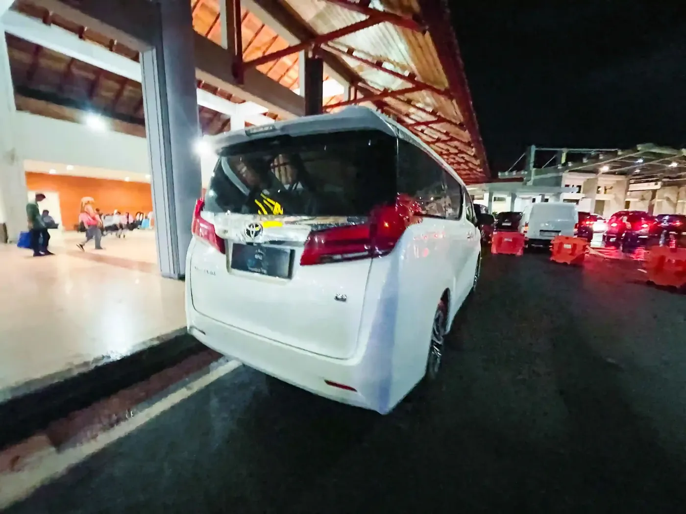 A white Alphard in the airport pick-up lane at night