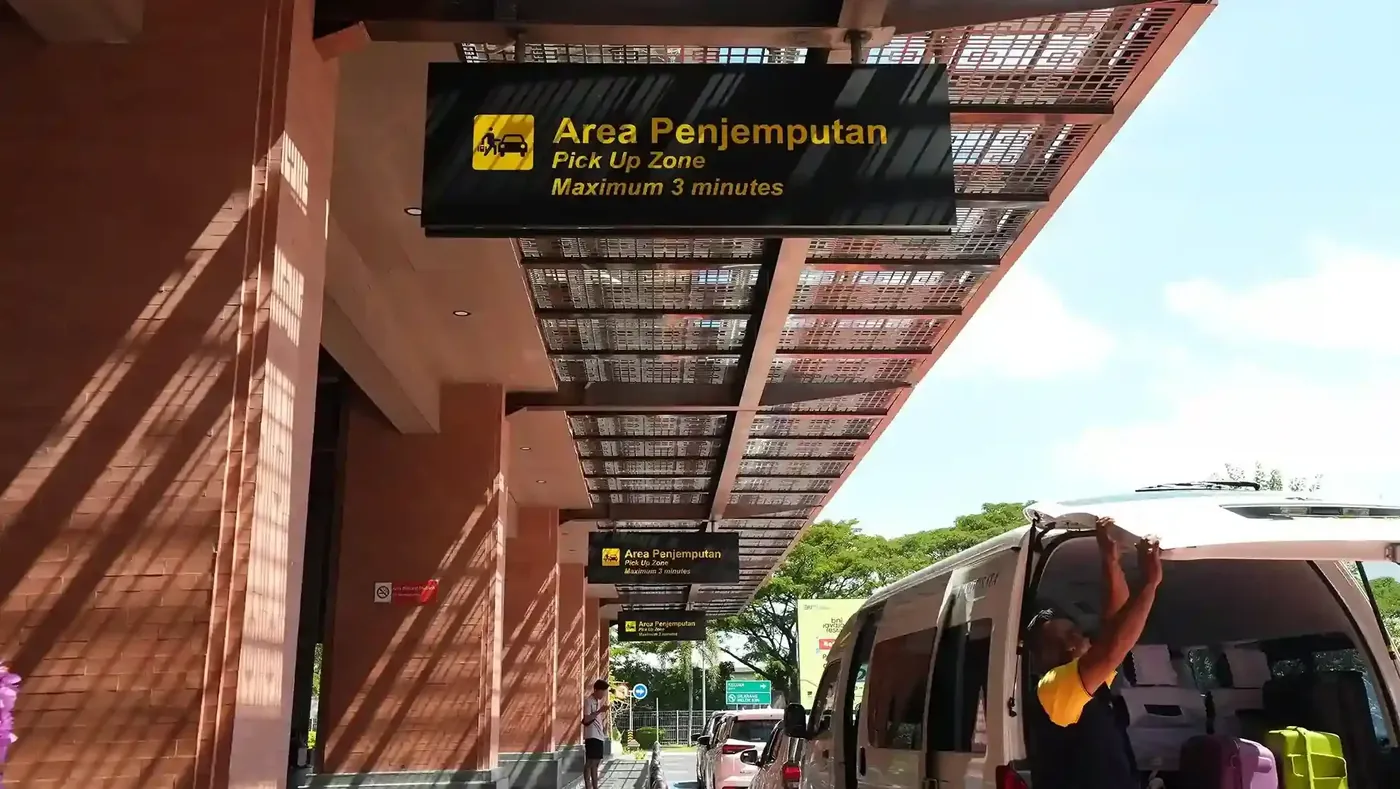 The Area Penjemputan pick-up zone sign at Ngurah Rai airport, with a vehicle at the kerb