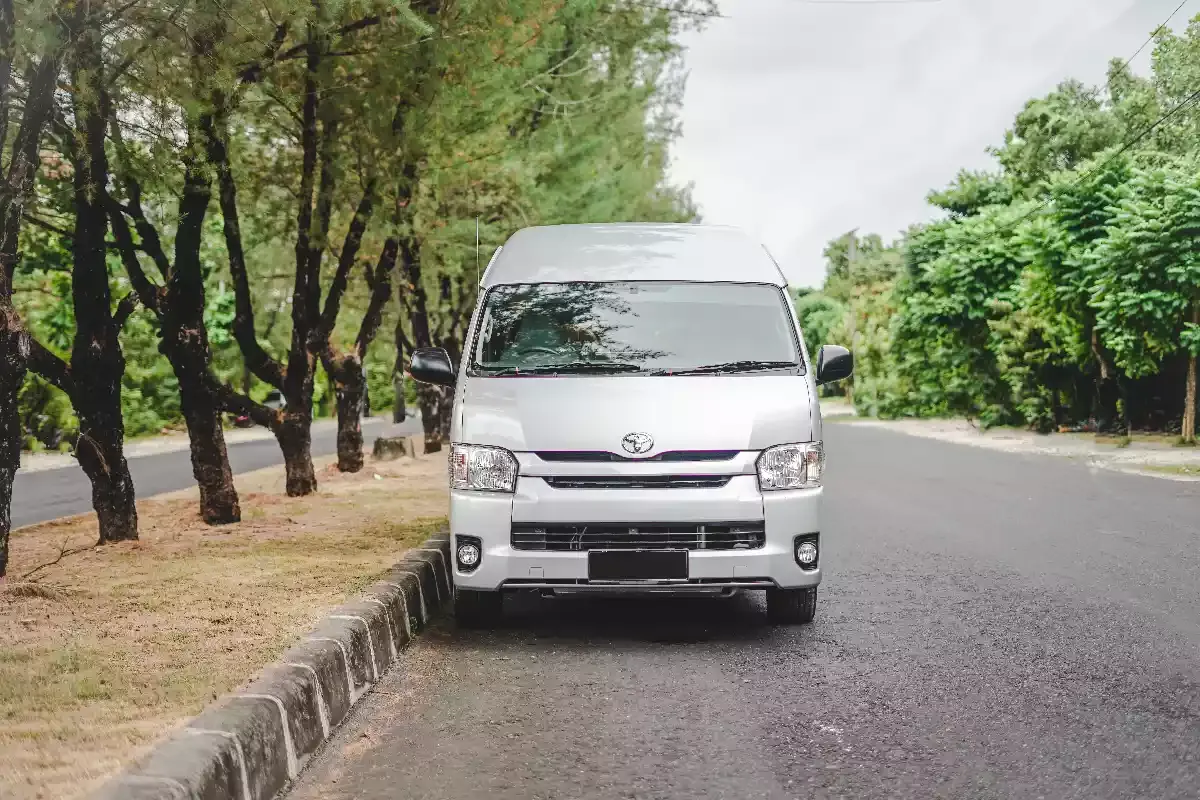 A white Toyota HiAce on a tree-lined road